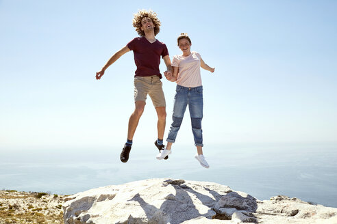 South Africa, Cape Town, happy young couple jumping on top of a mountain at the coast - SRYF00744