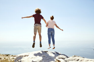 Südafrika, Kapstadt, junges Paar springt auf einen Berg an der Küste - SRYF00745