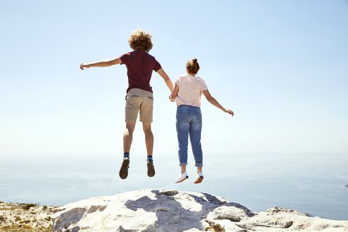 South Africa, Cape Town, young couple jumping on top of a mountain at the coast - SRYF00745