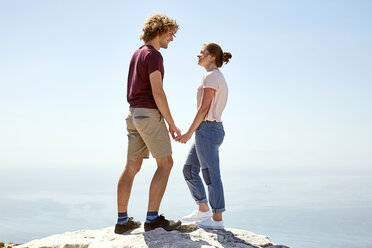 South Africa, Cape Town, young couple standing on top of a mountain at the coast holding hands - SRYF00746