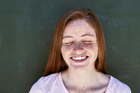 Portrait of smiling young woman with freckles closing her eyes stock photo