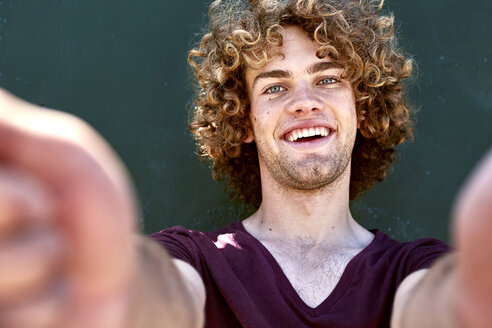 Portrait of laughing young man with curly hair in front of a green wall - SRYF00758