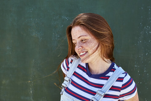 Smiling young woman with freckles in front of green wall - SRYF00764