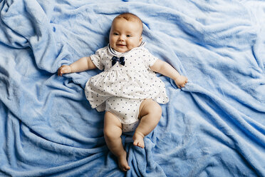 Porträt eines lächelnden kleinen Mädchens, das auf einer hellblauen Decke liegt - JRFF01490