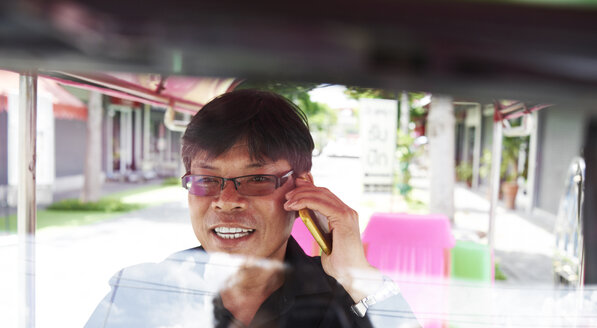 Thailand, Bangkok, Tuk-Tuk-Fahrer, der mit dem Handy telefoniert - IGGF00347