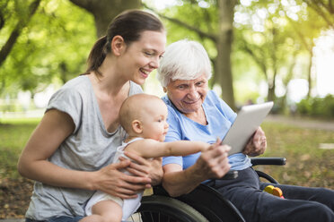 Grandmother, daughter and granddaughter having fun with tablet in a park - DIGF03211