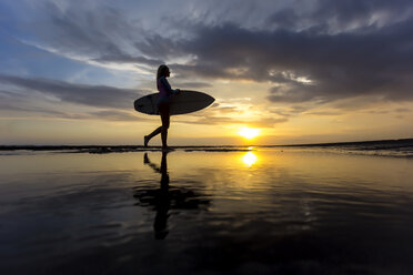 Indonesia, Bali, young woman with surfboard at sunset - KNTF00952