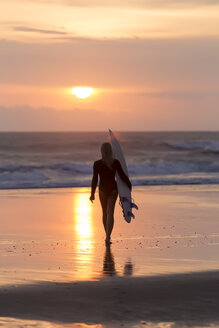 Indonesien, Bali, junge Frau mit Surfbrett bei Sonnenuntergang - KNTF00954