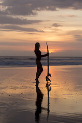 Indonesien, Bali, junge Frau mit Surfbrett bei Sonnenuntergang - KNTF00955