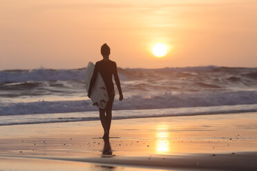 Indonesia, Bali, young woman with surfboard at sunset - KNTF00968