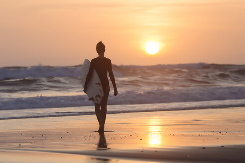 Indonesien, Bali, junge Frau mit Surfbrett bei Sonnenuntergang - KNTF00968