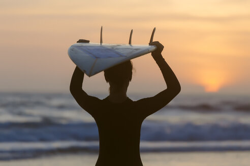 Indonesien, Bali, junge Frau mit Surfbrett auf dem Kopf bei Sonnenuntergang - KNTF00971