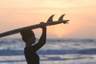 Indonesien, Bali, junge Frau mit Surfbrett auf dem Kopf bei Sonnenuntergang - KNTF00972