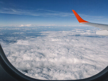 Red wing of airplane flying over clouds in the sky. - BZF00379