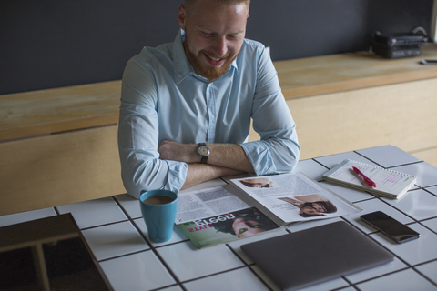 Lächelnder Mann, der zu Hause Kaffee trinkt und eine Zeitschrift liest, lizenzfreies Stockfoto