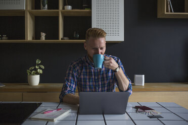 Mann trinkt Kaffee und benutzt Laptop zu Hause - MOMF00355