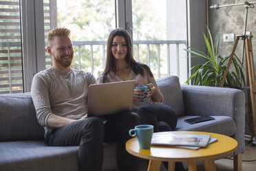 Couple sitting on couch looking at laptop - MOMF00361