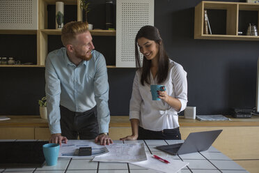 Smiling man and woman with plans on table at home - MOMF00373