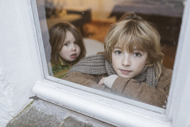 Porträt eines Jungen, der aus dem Fenster schaut, mit seiner kleinen Schwester im Hintergrund - KMKF00123