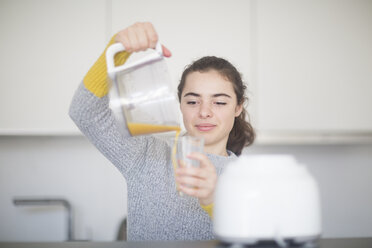 Porträt einer lächelnden Frau, die in der Küche frisch gepressten Orangensaft in ein Glas gießt - SGF02135