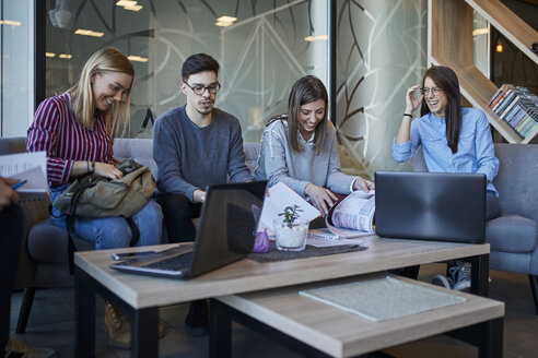 Eine Gruppe von Freunden sitzt in einem Café mit Laptop und Dokumenten zusammen - ZEDF01034