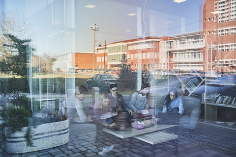 Gruppe von Freunden sitzt zusammen in einem Café mit Reflexion der Glasscheibe, lizenzfreies Stockfoto