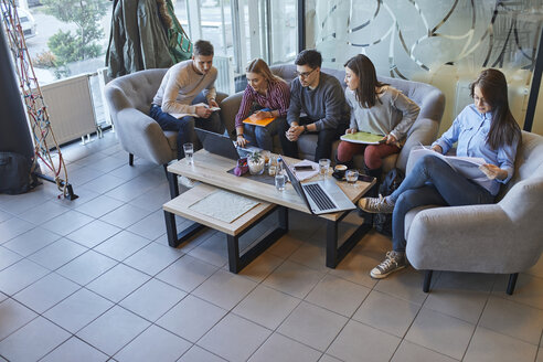 Eine Gruppe von Freunden sitzt in einem Café mit Laptop und Dokumenten zusammen - ZEDF01044