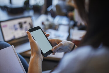 Junge Frau in einem Café, die ein Smartphone mit einem Laptop im Hintergrund benutzt - ZEDF01049