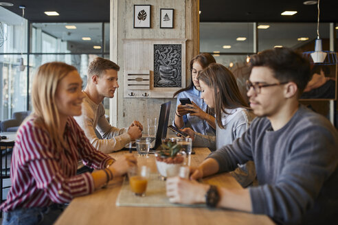 Eine Gruppe von Freunden sitzt mit Laptop, Smartphones und Getränken in einem Café zusammen - ZEDF01054