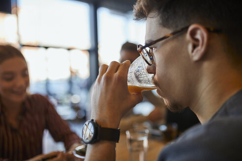 Junger Mann trinkt ein Glas Saft in einem Cafe mit Freunden im Hintergrund - ZEDF01057