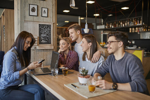 Eine Gruppe von Freunden sitzt mit Laptop, Smartphone und Getränken in einem Café zusammen - ZEDF01060
