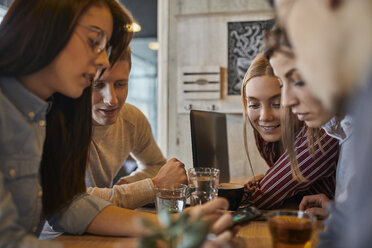 Eine Gruppe von Freunden sitzt zusammen in einem Café und teilt sich ein Smartphone - ZEDF01063