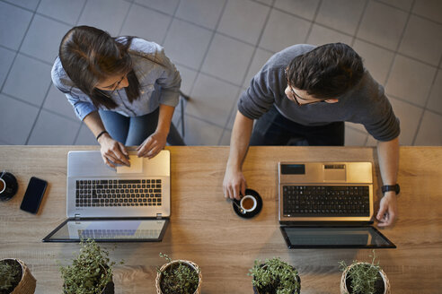 Draufsicht auf eine junge Frau und einen Mann in einem Café mit Laptops, die sich unterhalten - ZEDF01067