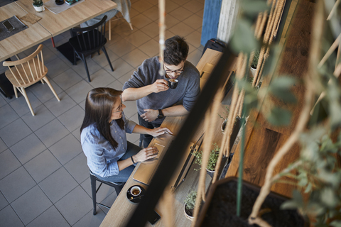 Junge Frau und Mann in einem Café mit Laptops, die sich unterhalten und Espresso trinken, lizenzfreies Stockfoto