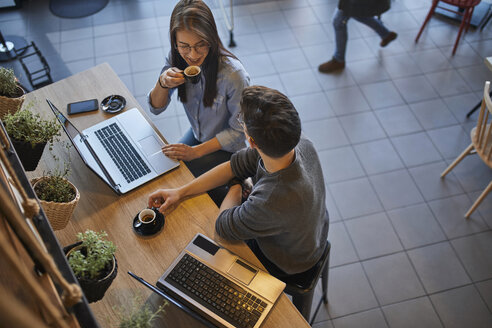 Junge Frau und Mann in einem Café mit Laptops, die sich unterhalten und Espresso trinken - ZEDF01073