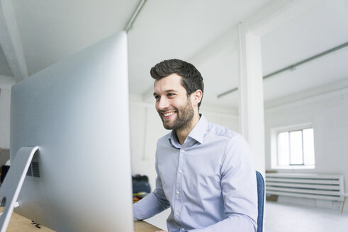 Lächelnder Geschäftsmann bei der Arbeit am Schreibtisch im Büro - MOEF00639