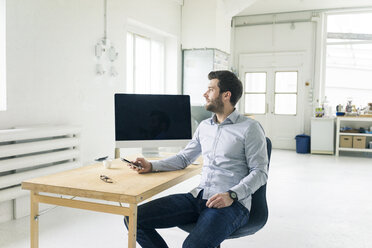 Businessman with cell phone sitting at desk in office - MOEF00641