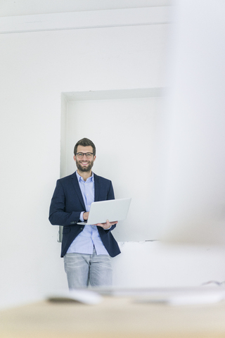 Portrait of smiling businessman with laptop in office stock photo