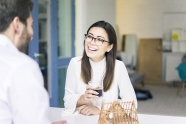 Woman laughing at man with architectural model on table - MOEF00650