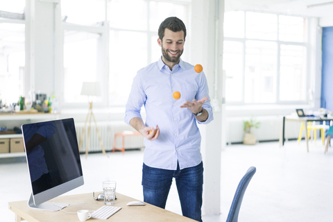 Smiling businessman juggling with tangerines in office stock photo