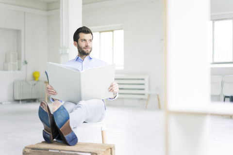 Businessman sitting in empty loft office holdig large folder stock photo