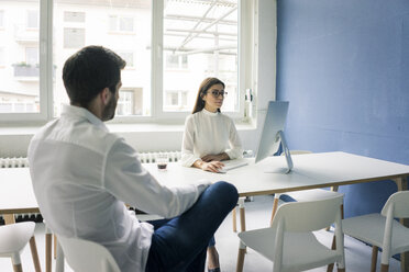 Mann sitzt einer Frau gegenüber, die im Büro einen Computer benutzt - MOEF00665