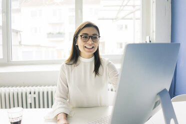 Lächelnde Geschäftsfrau bei der Arbeit am Schreibtisch im Büro - MOEF00667