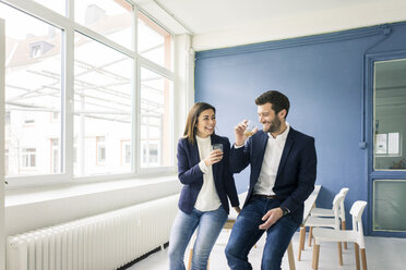 Happy businessman and businesswoman with drinks in office - MOEF00668