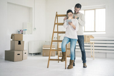 Laughing couple at ladder in new home looking at tablet - MOEF00676