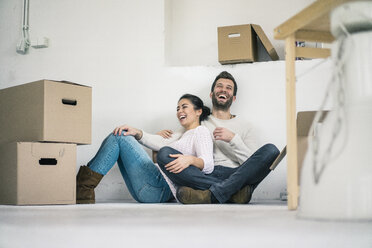 Laughing couple sitting in new home surrounded by cardboard boxes - MOEF00684