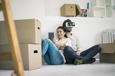 Ehepaar sitzt in neuem Haus mit Mann, der eine VR-Brille trägt - MOEF00685