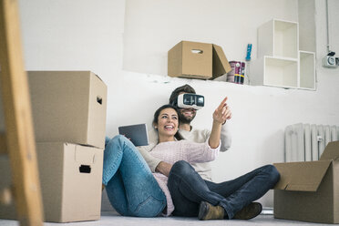 Couple sitting in new home with man wearing VR glasses - MOEF00686