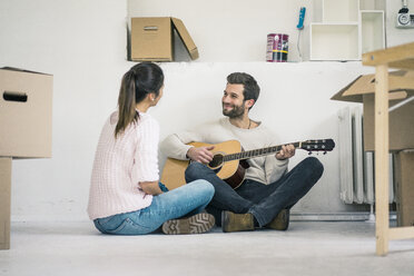 Couple sitting on the floor in new home playing guitar - MOEF00690