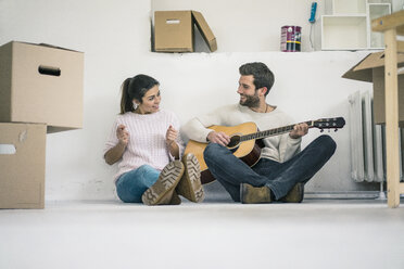 Couple sitting on the floor in new home playing guitar - MOEF00691